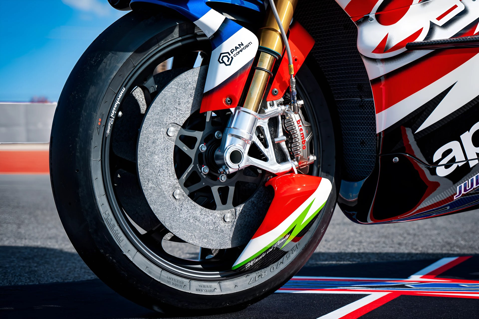 Close-up of a motorcycle front wheel with Brembo brake caliper and Pan Compositi fork on a racetrack.