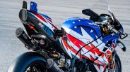 Blue, red, and white Aprilia racing motorcycle with SC Project dual exhausts on a racetrack.