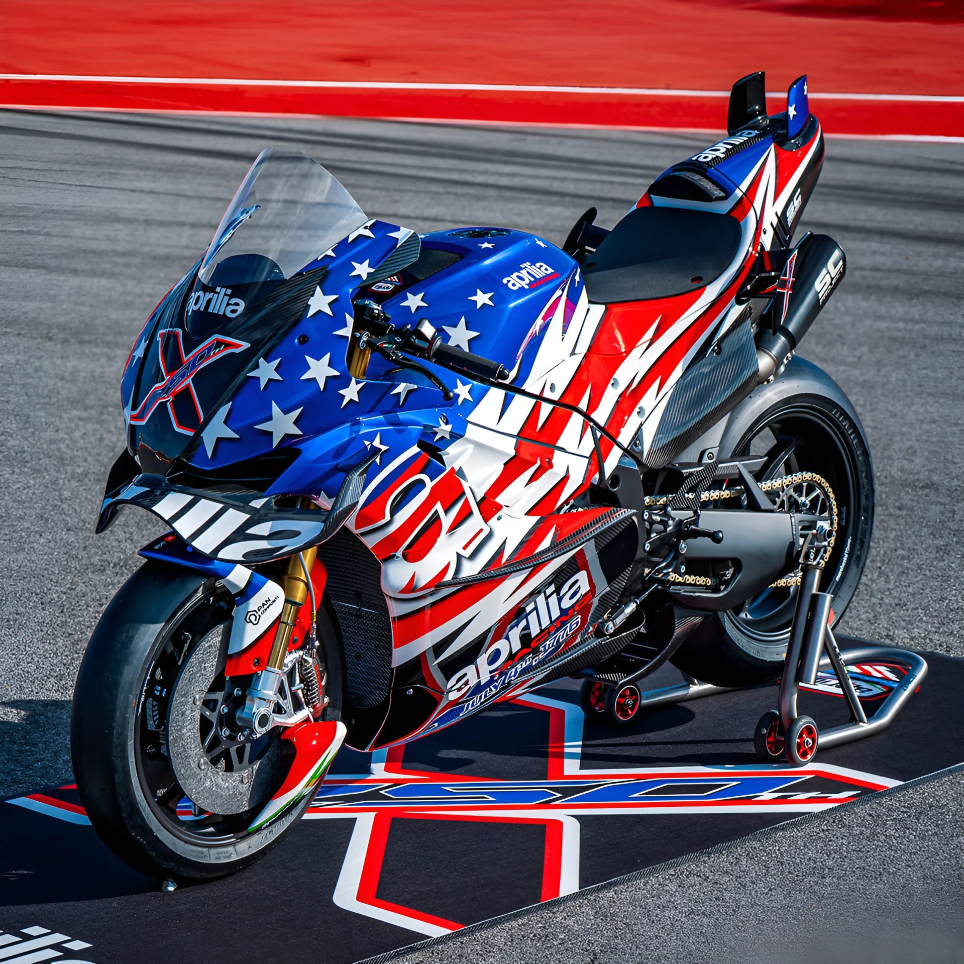 Race-ready Aprilia sport motorcycle with red, white, and blue star-spangled livery on a track mat.