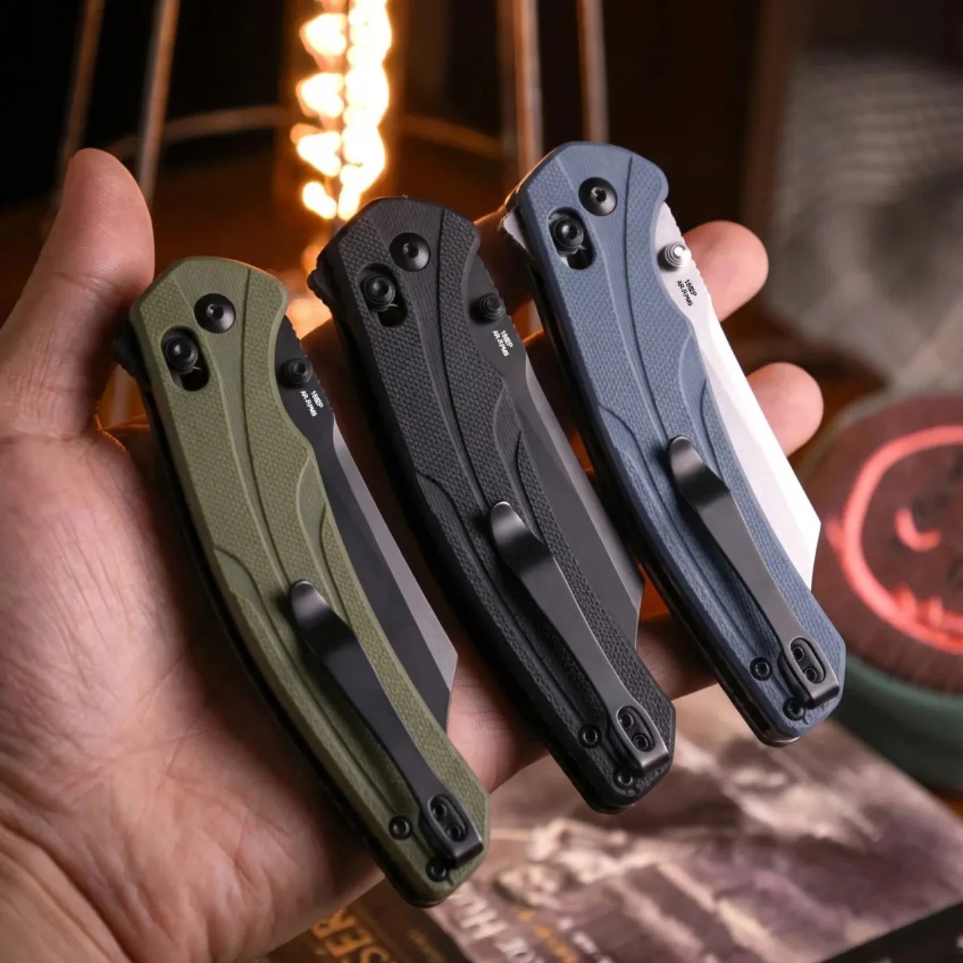 Three closed folding knives with textured handles in green, black, and blue held in a hand.