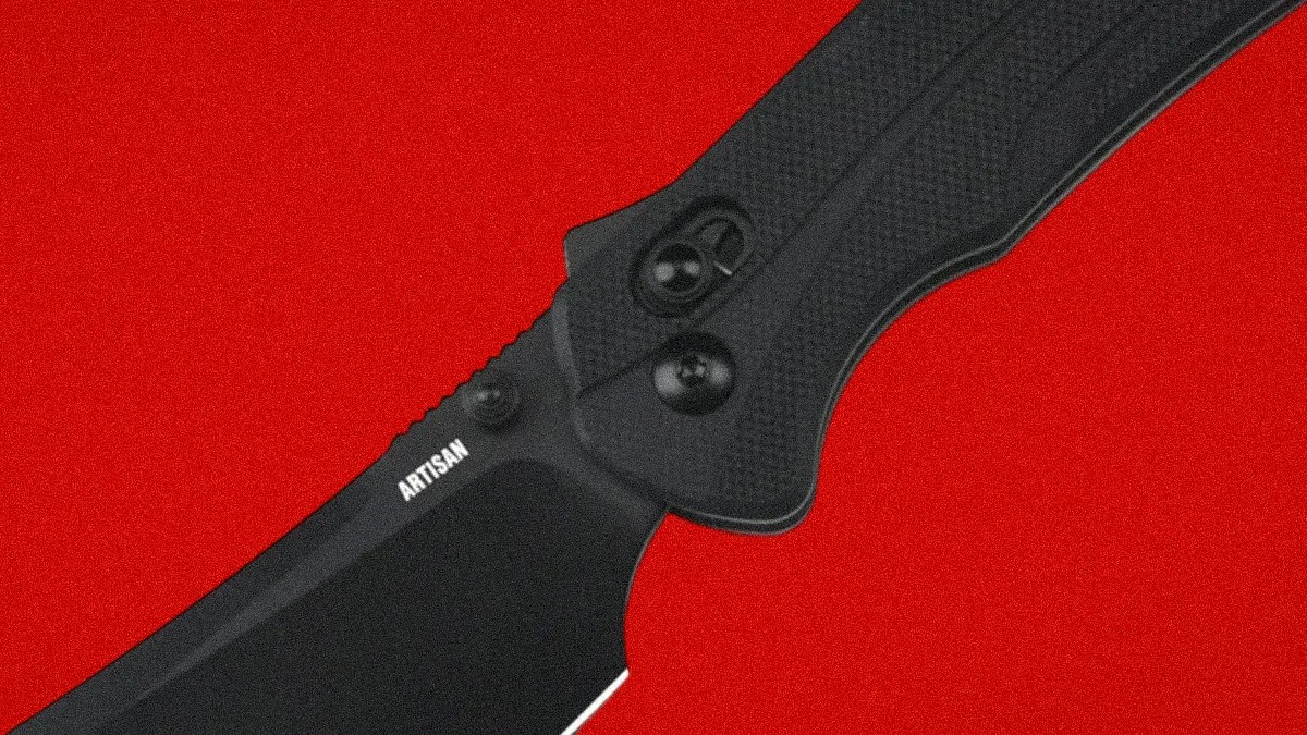 Close-up of a black folding knife blade with "ARTISAN" text and textured black handle on a red background.