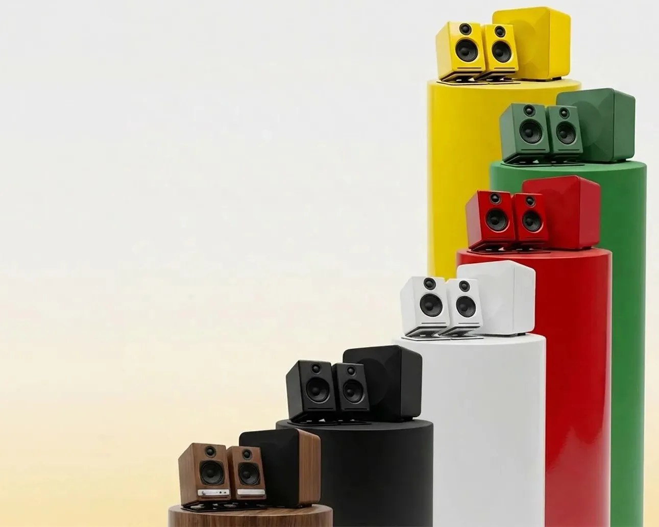 Five sets of compact speakers and subwoofers in wood, black, white, red, green, and yellow colors arranged on matching cylindrical pedestals.