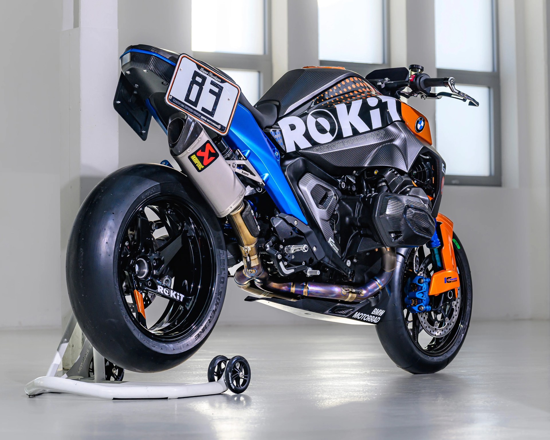 Black and orange BMW racing motorcycle with ROKiT branding on a white stand in a bright room.