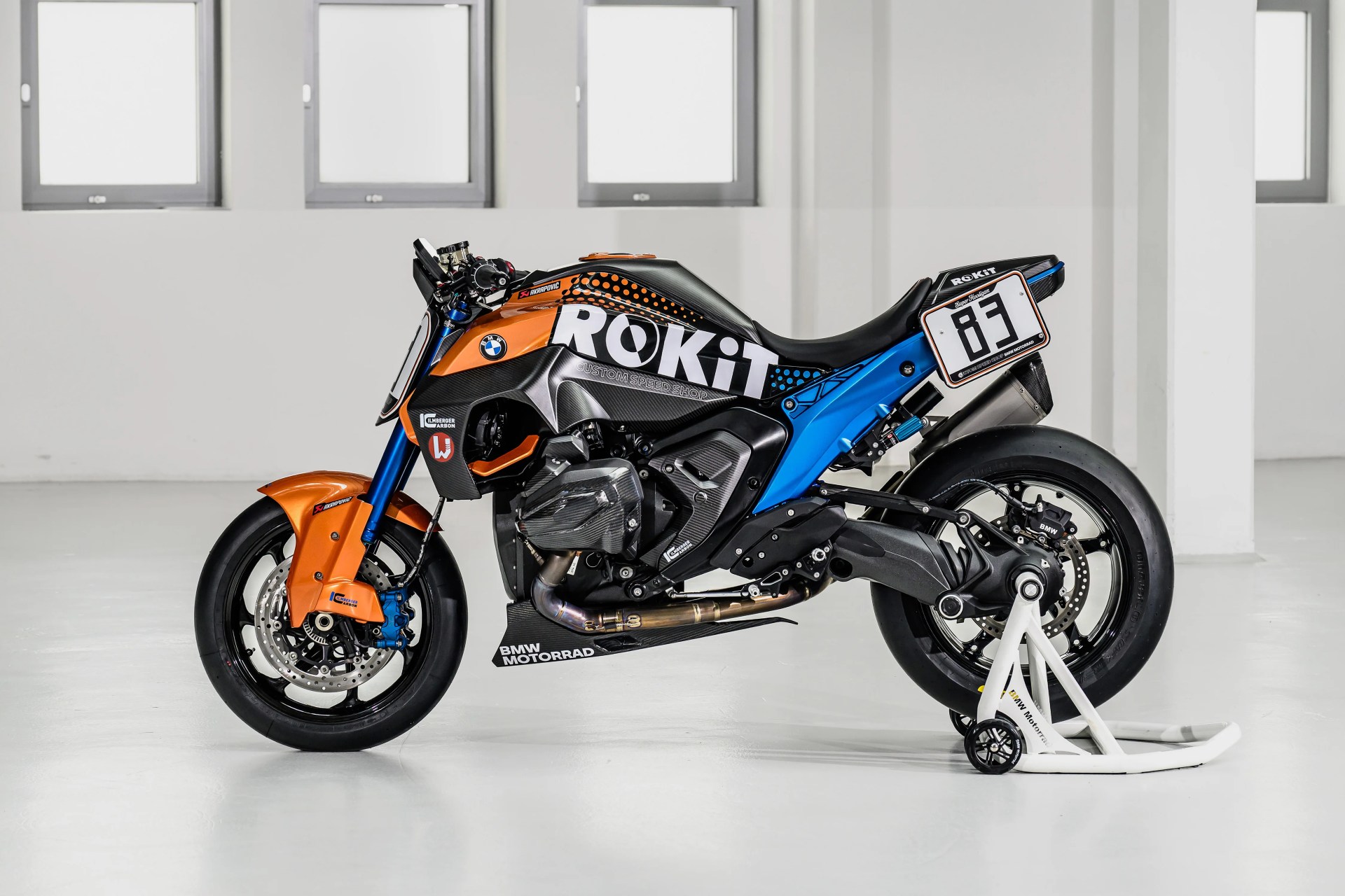 Sport motorcycle with orange, blue, and black bodywork, "ROKiT" branding, and number 83 plate on a white stand.