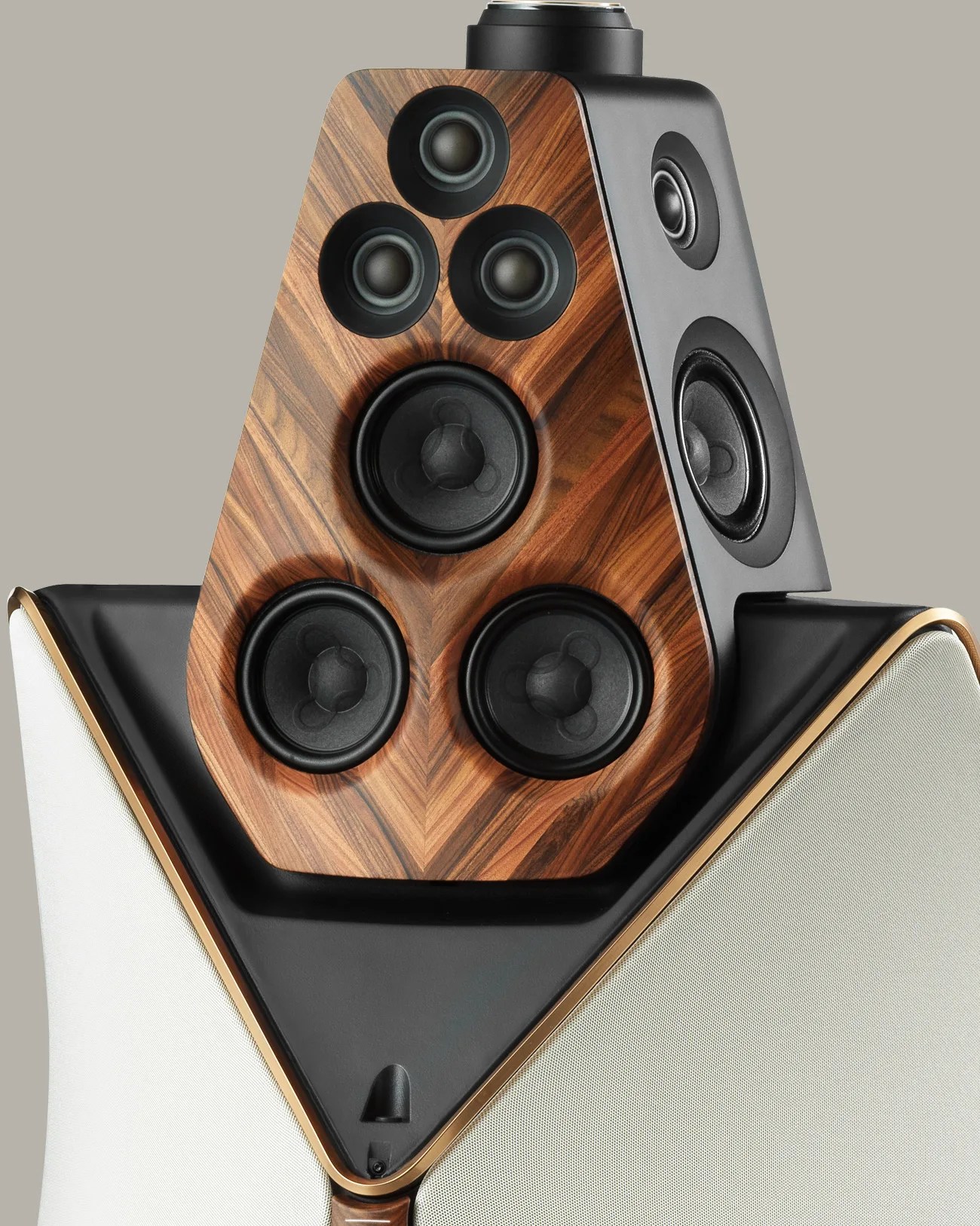 High-end speaker with multiple black drivers on a wood veneer and black panel, white fabric sides, and gold trim.