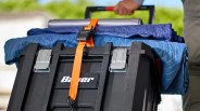 Black plastic toolbox with silver latches secured by an orange strap holding blue moving blankets on top.