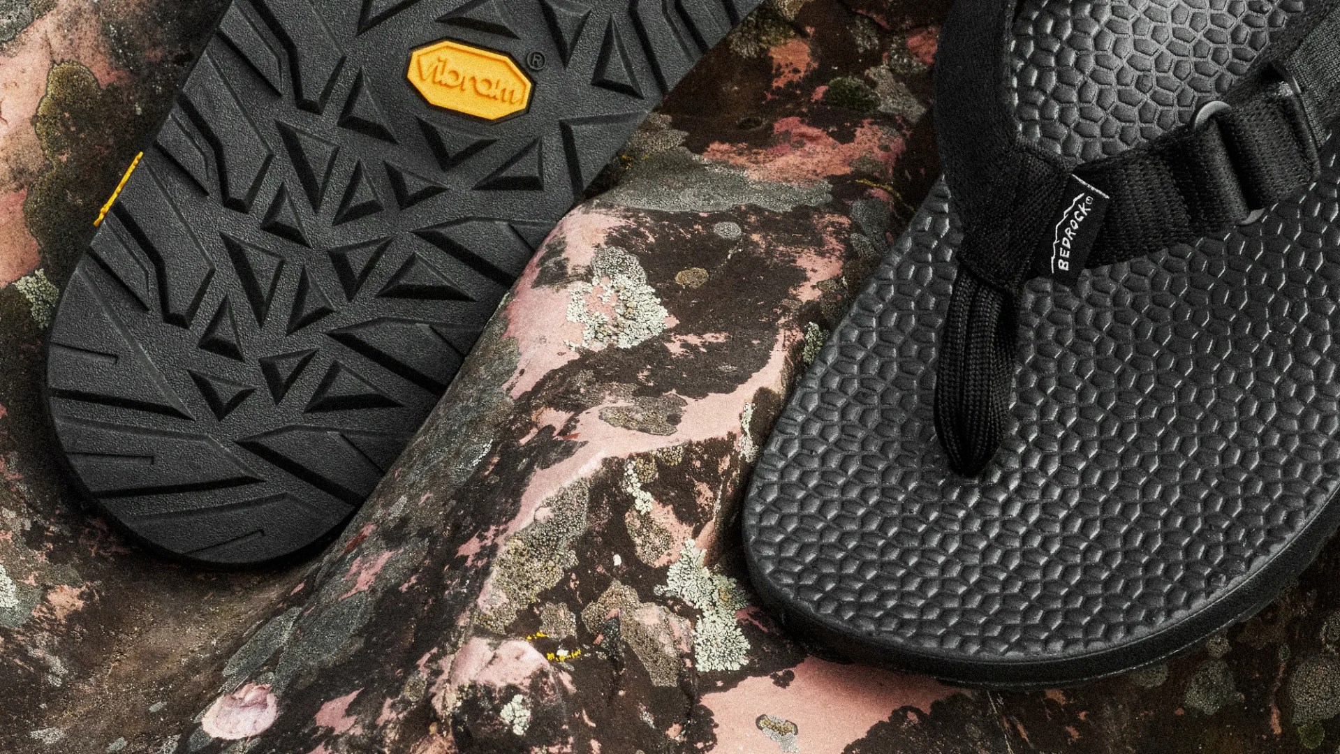 Close-up of black textured flip-flops with "Bedrock" tag and Vibram sole on a lichen-covered rock surface.