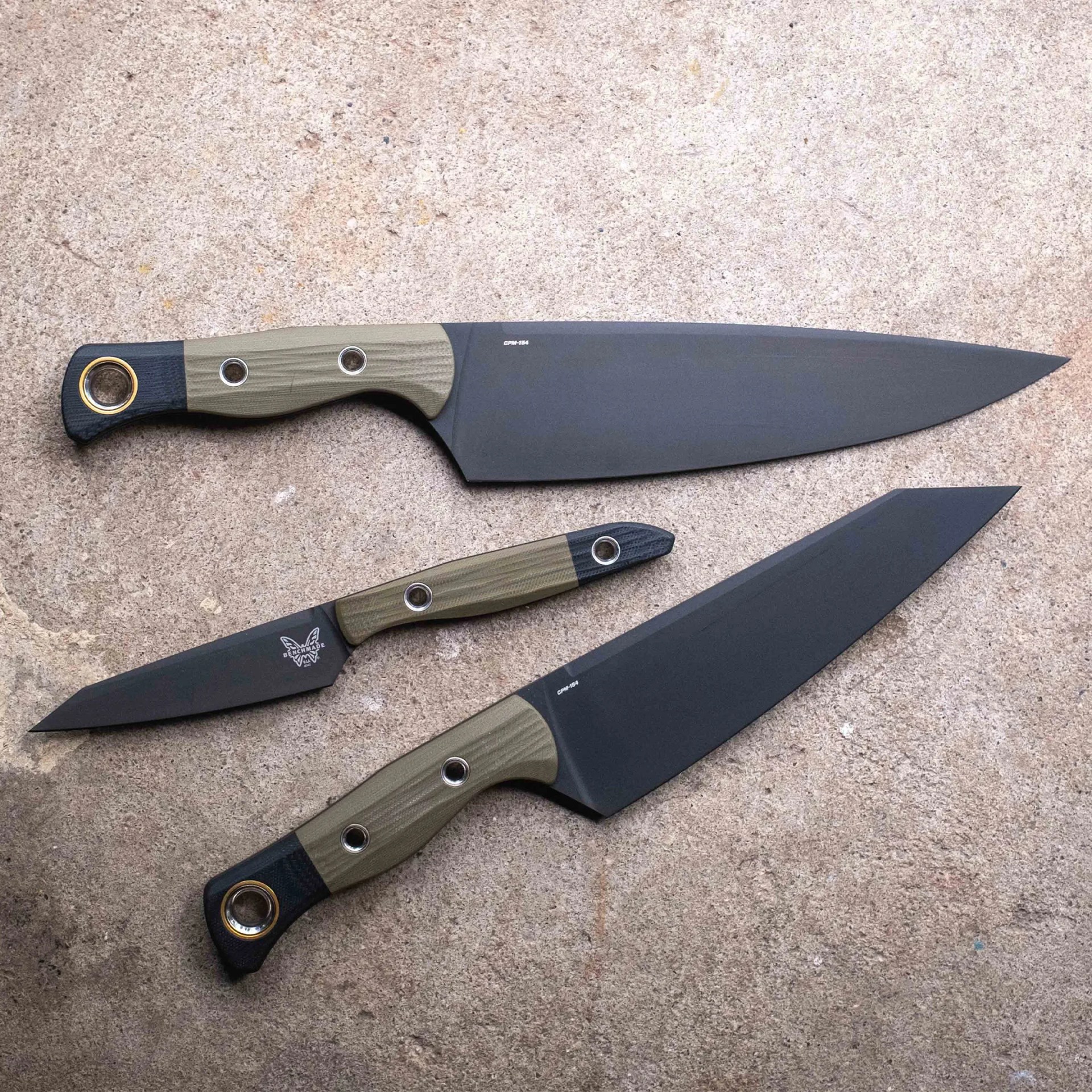 Three black-bladed knives with green and black handles laid on a textured surface.