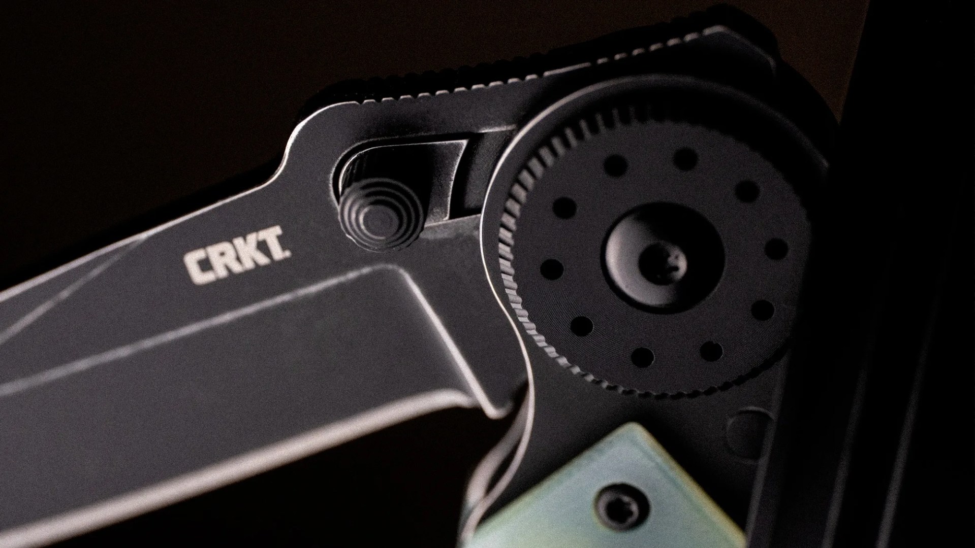 Close-up of a black CRKT folding knife showing the pivot mechanism and thumb stud.