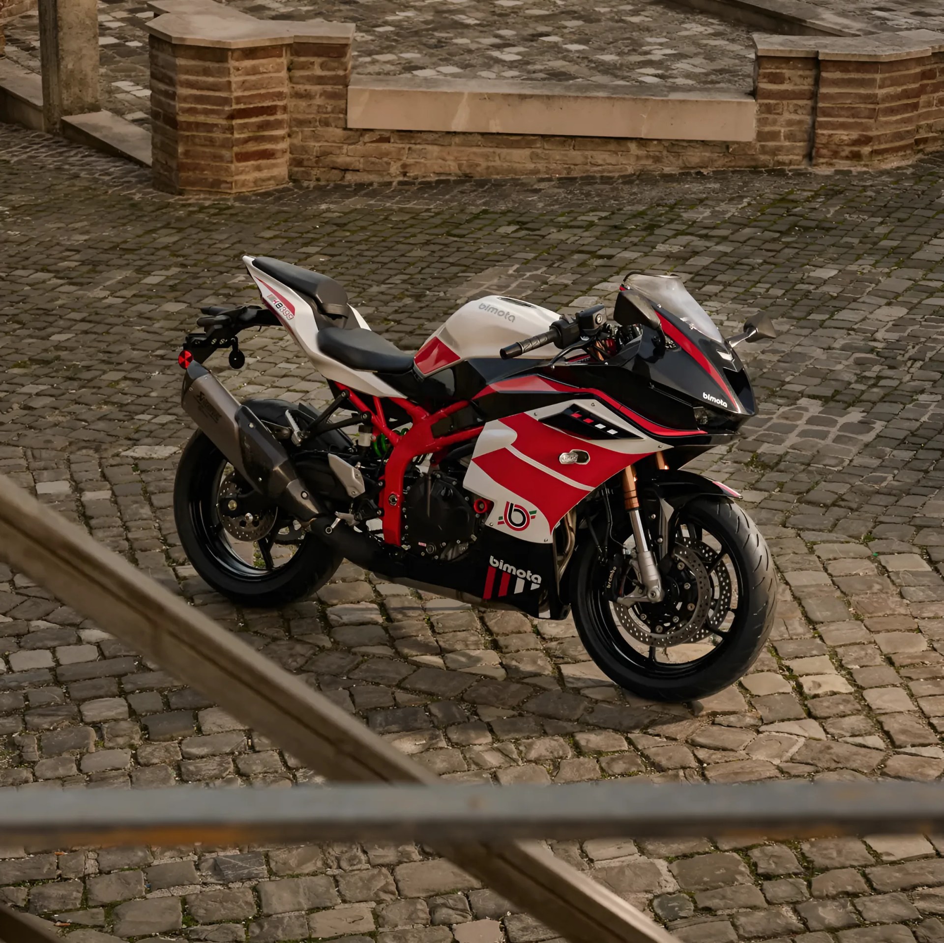 Red, white, and black Bimota sport motorcycle parked on a cobblestone surface near brick steps.