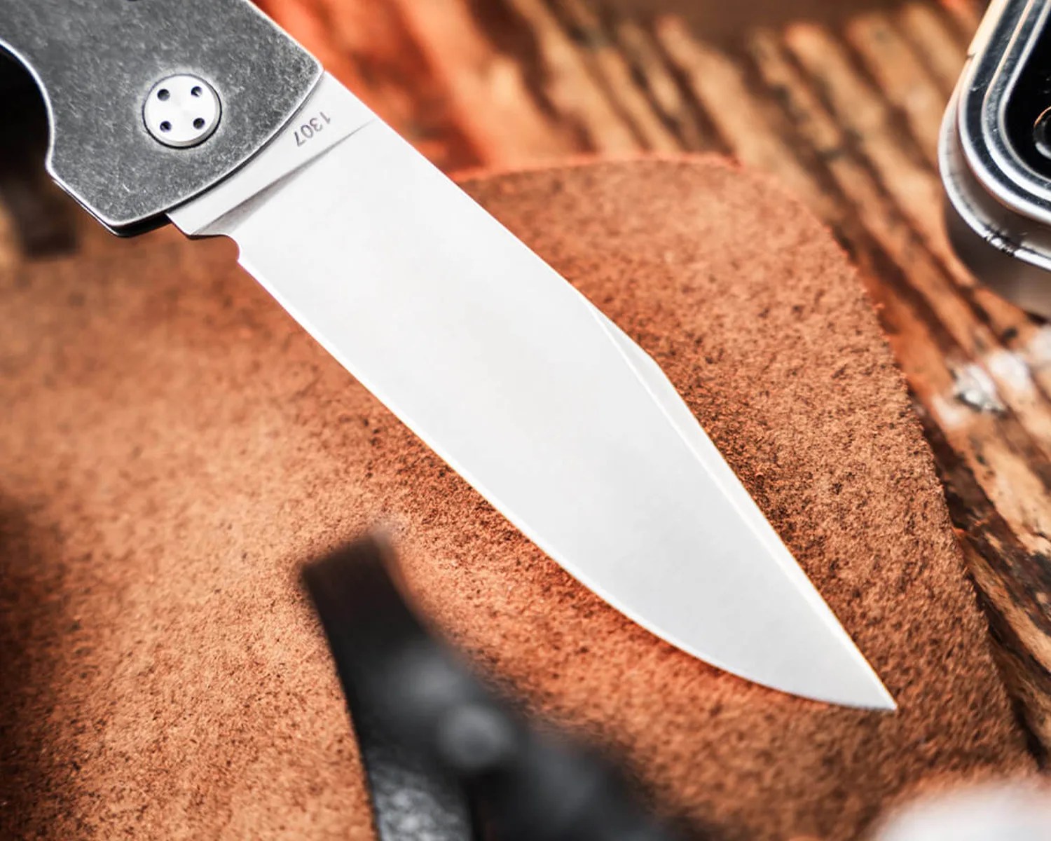 Close-up of a stainless steel knife blade with the number 1307 engraved near the handle, resting on a brown textured surface.