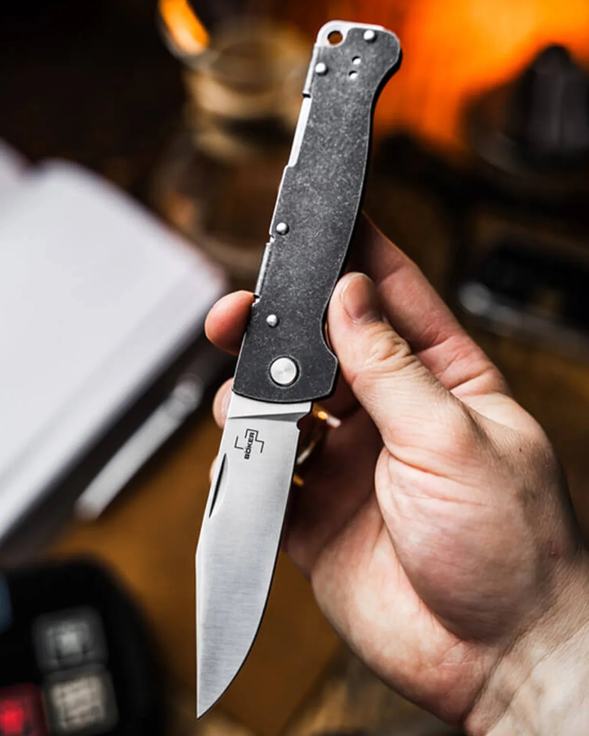 Hand holding a folding knife with a stonewashed black handle and a satin-finished blade.