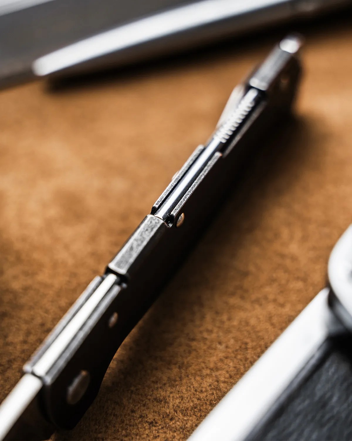 Close-up of a folding knife's metal hinge and black handle on a brown surface.