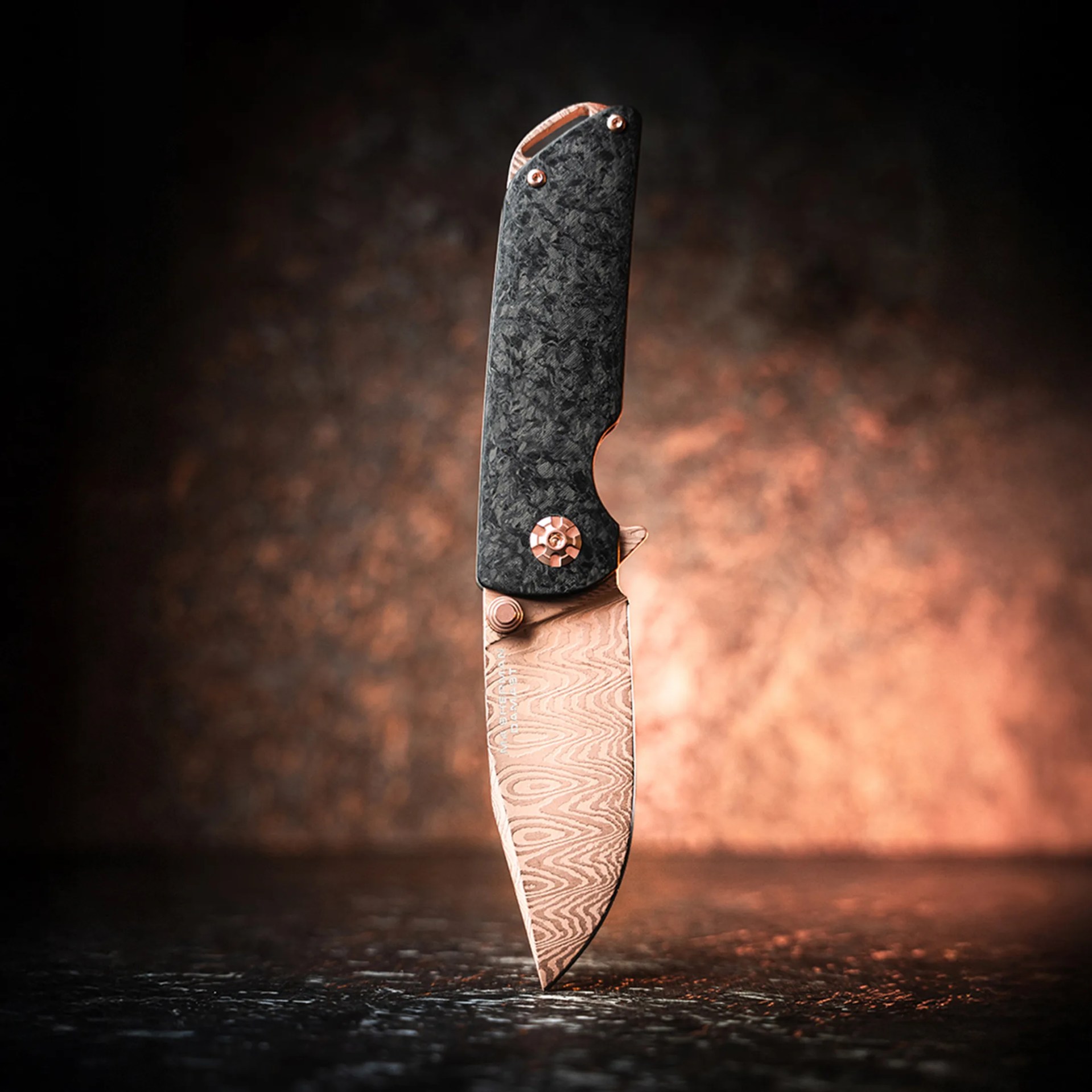Folding knife with a patterned copper blade and black textured handle standing upright on a dark surface.