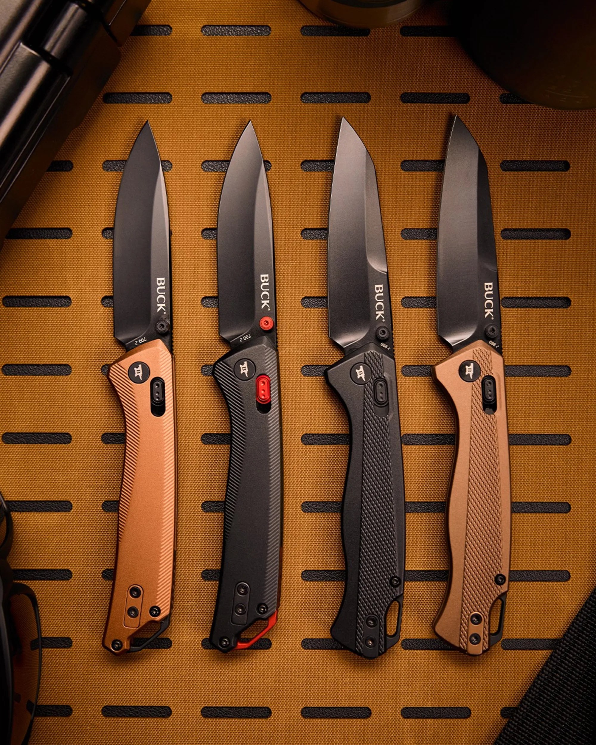 Four Buck folding knives with black blades and textured handles in tan and black colors, arranged on a brown surface.