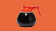 Glass coffee carafe with bright orange plastic lid and handle filled with black coffee.