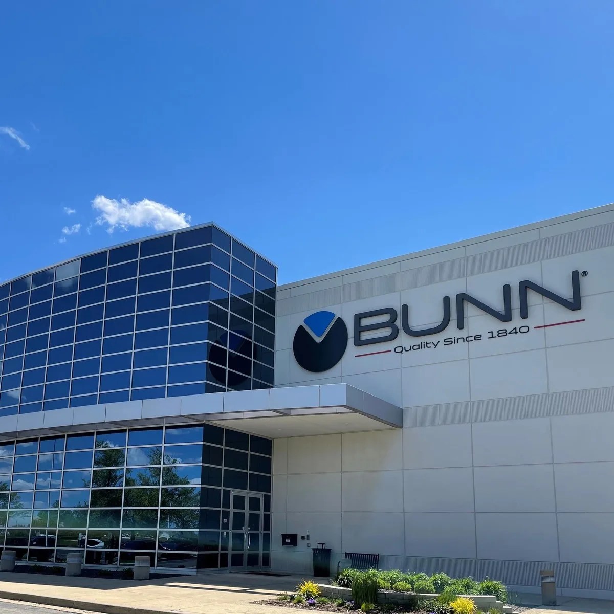 Modern commercial building with large blue-tinted glass windows and a BUNN logo on the white exterior wall.