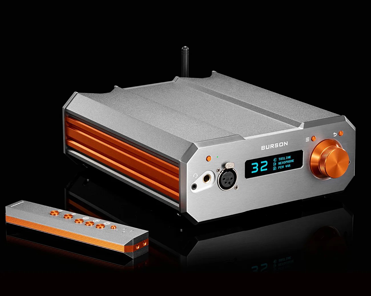 Silver and orange Burson audio amplifier with digital display and matching remote on a black reflective surface.