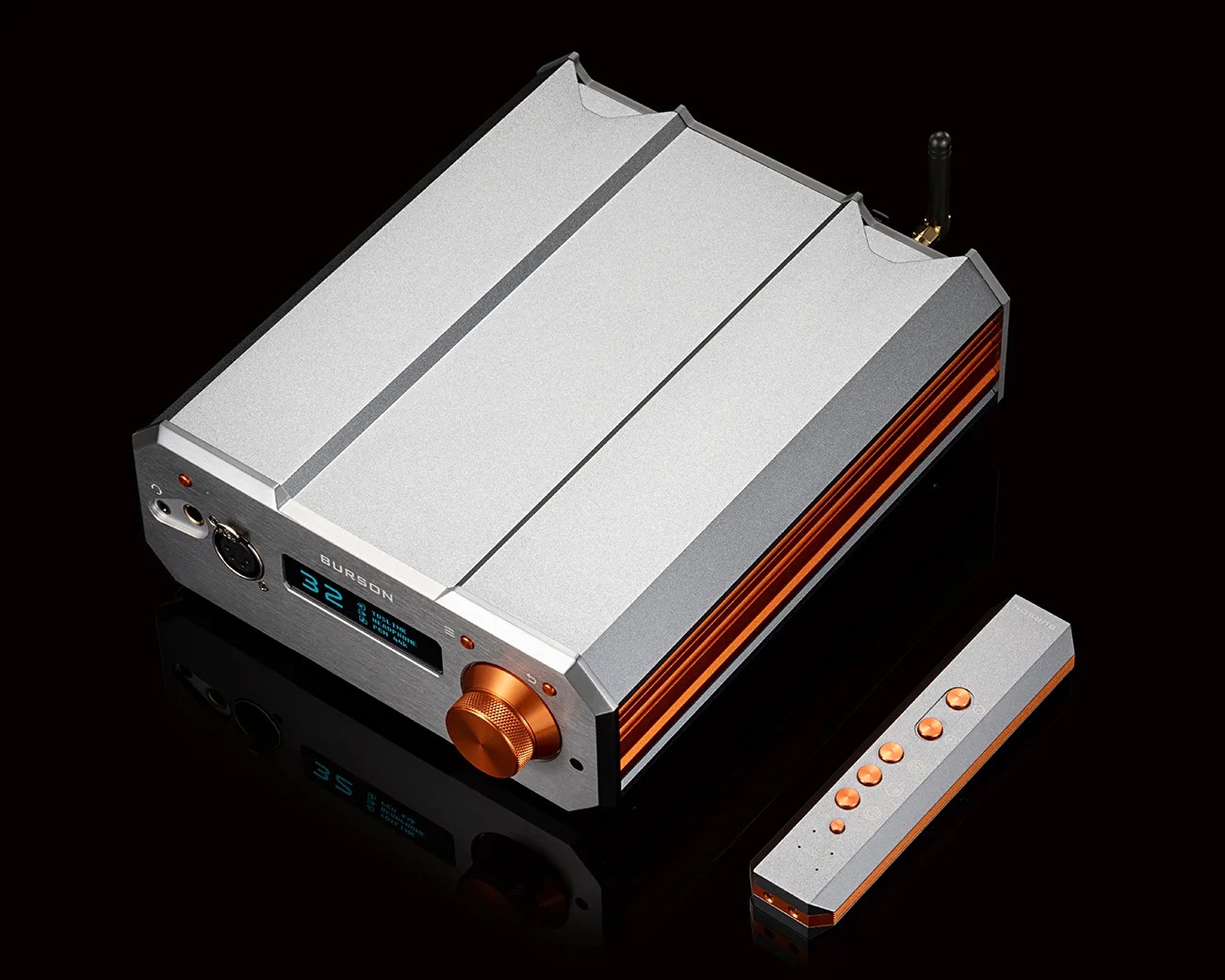 Silver and orange Burson audio amplifier with digital display and matching remote control on a black reflective surface.