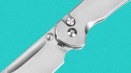 Close-up of a silver folding knife blade and handle with visible screws and a thumb stud on a turquoise background.