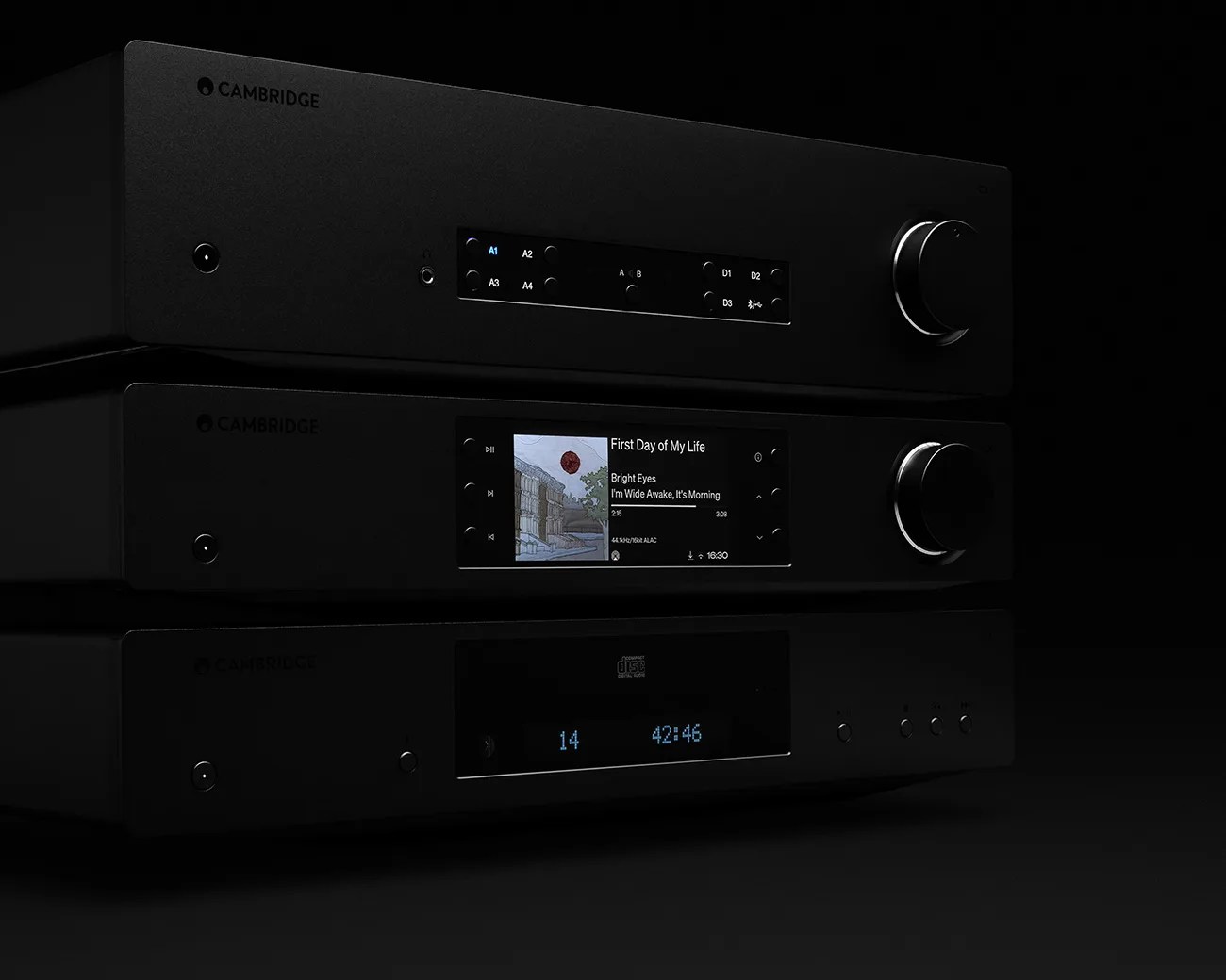 Three stacked black Cambridge audio components with digital displays and control knobs on a black background.