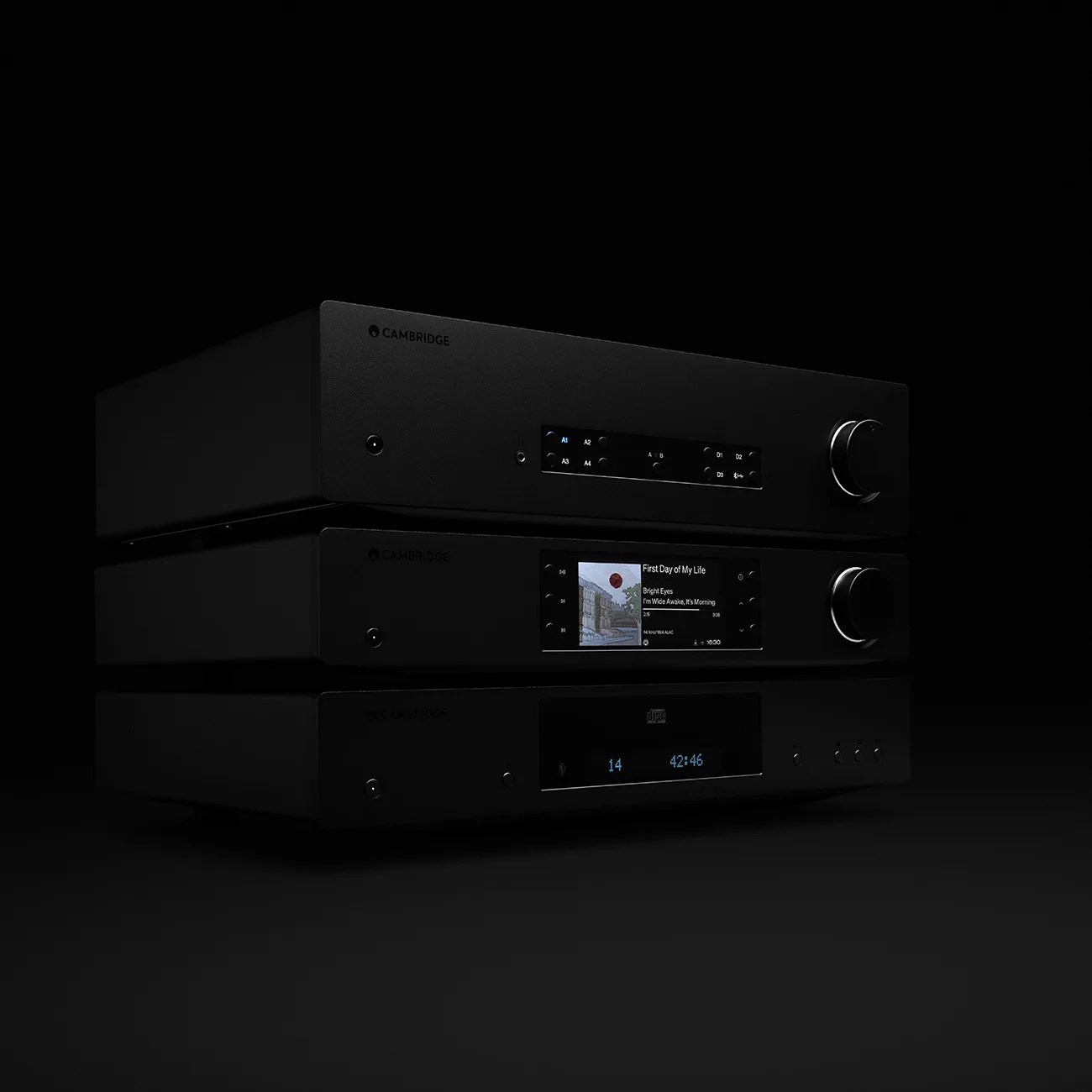 Three stacked black Cambridge audio components with digital displays, including a music player showing album art and track info.