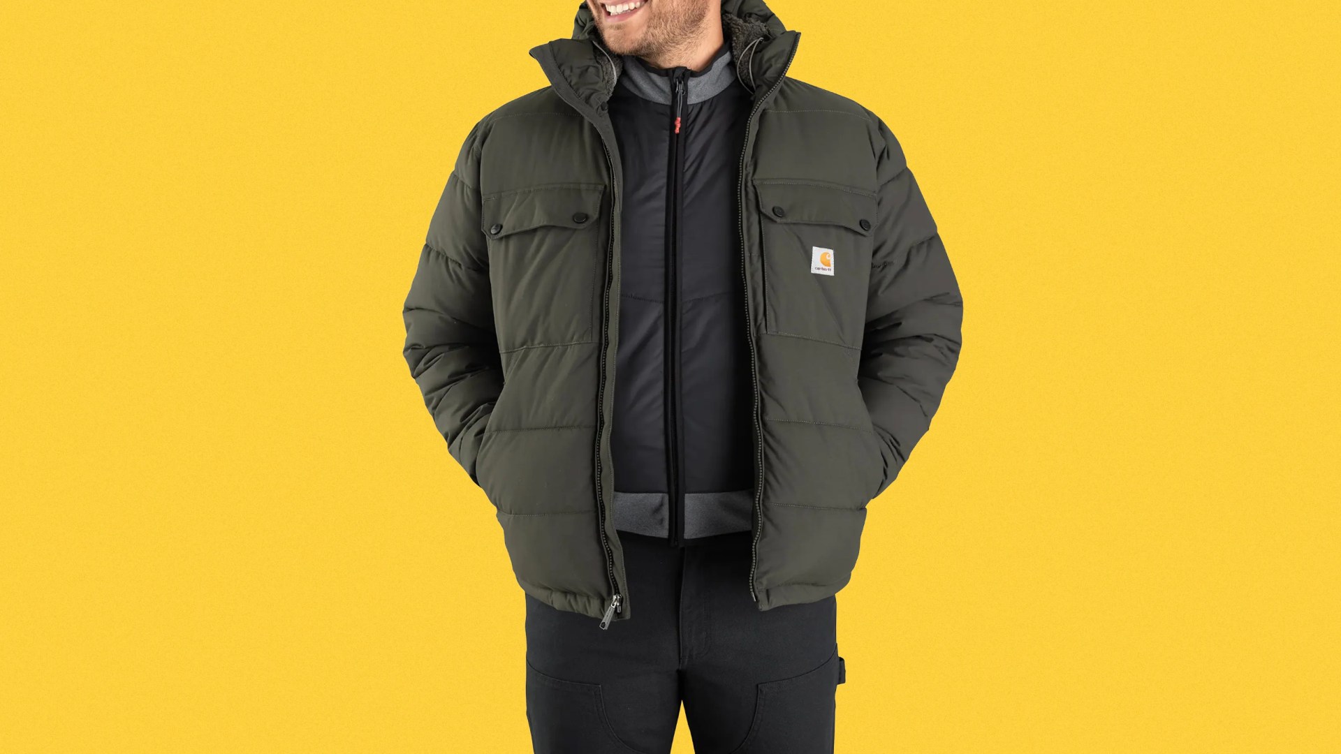 Olive green Carhartt puffer jacket with front pockets worn over a black zip-up jacket.
