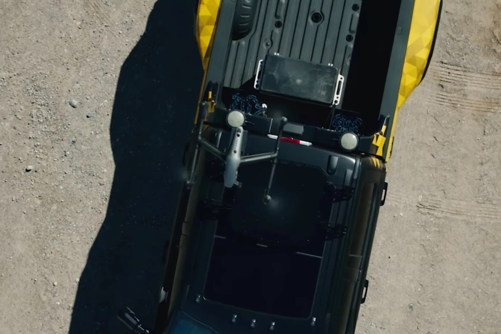 Drone flying over the bed of a yellow and black pickup truck on a dirt surface.