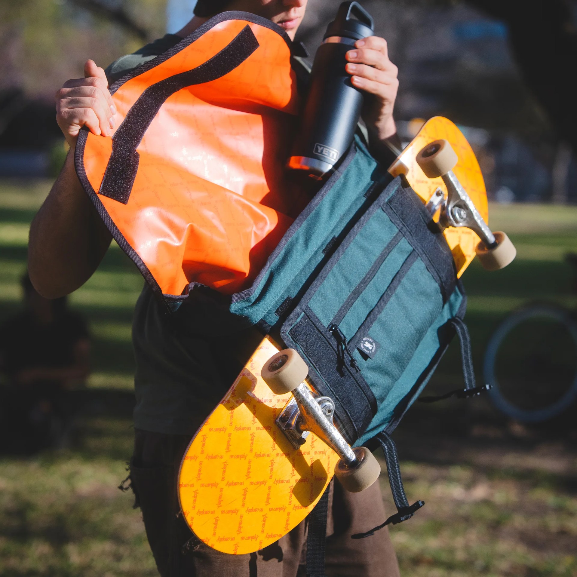 Green backpack with black zippers holding an orange skateboard and a black YETI water bottle.