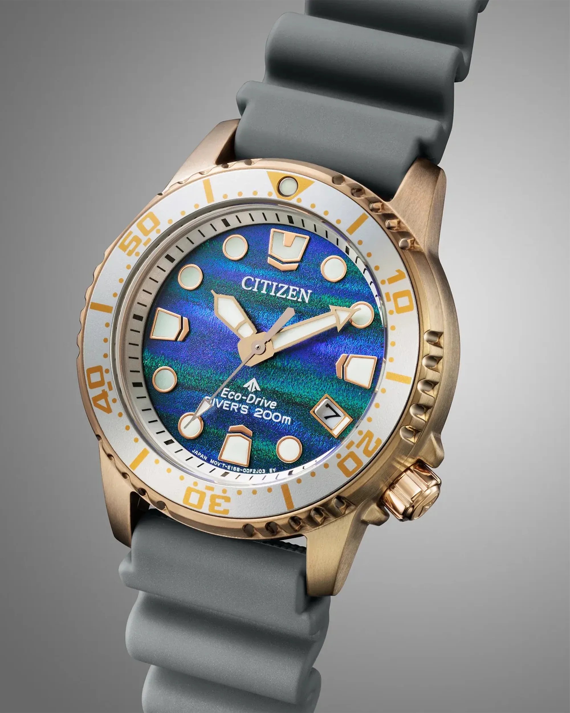 Citizen Eco-Drive diver's watch with blue-green dial, gold-tone case, white bezel, and gray rubber strap.