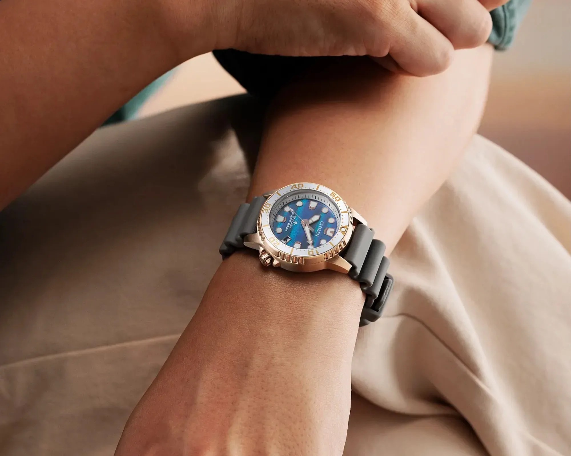 Wristwatch with a blue dial, gold bezel, and gray rubber strap worn on a wrist.