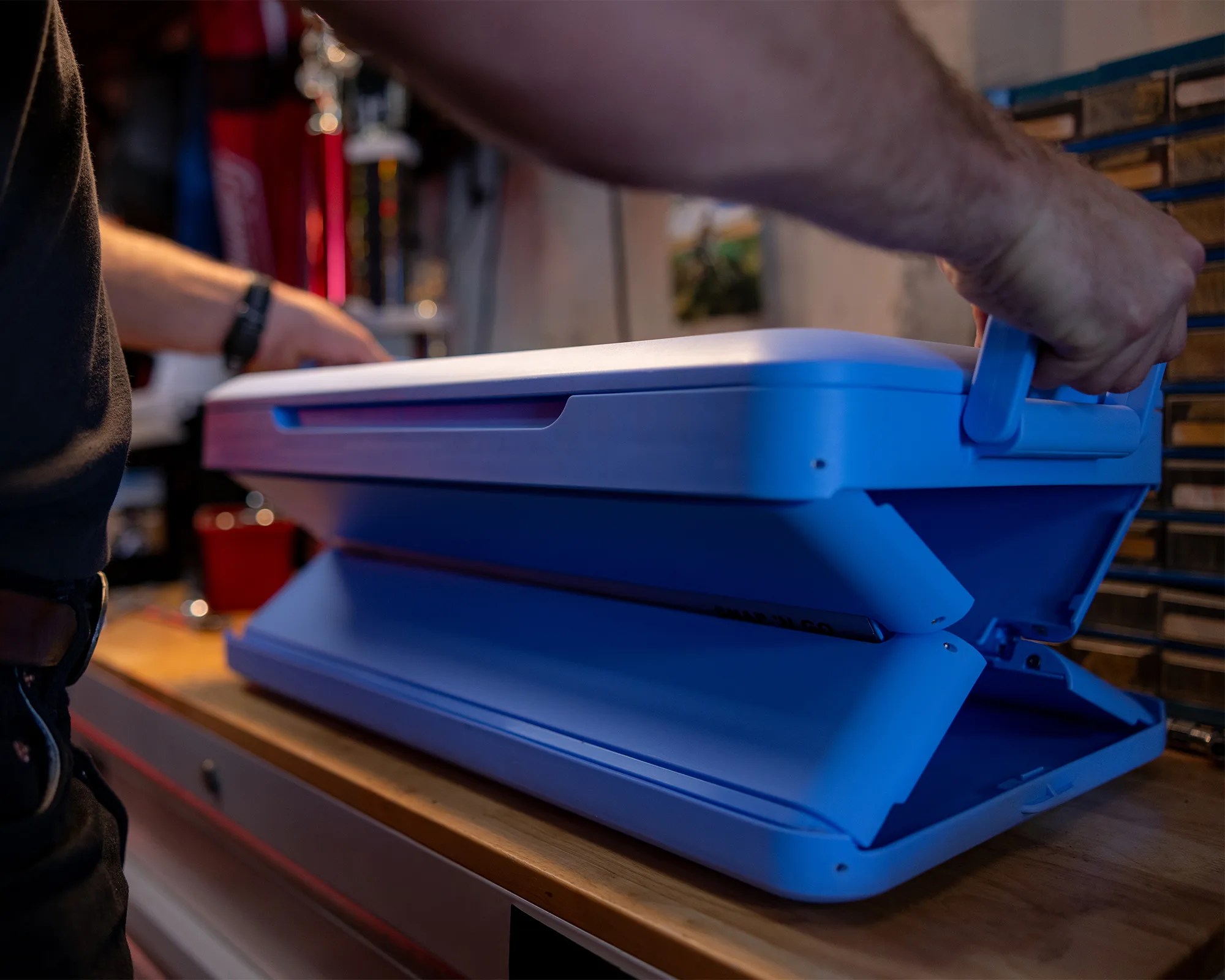 Blue plastic foldable cooler box being opened on a wooden workbench.