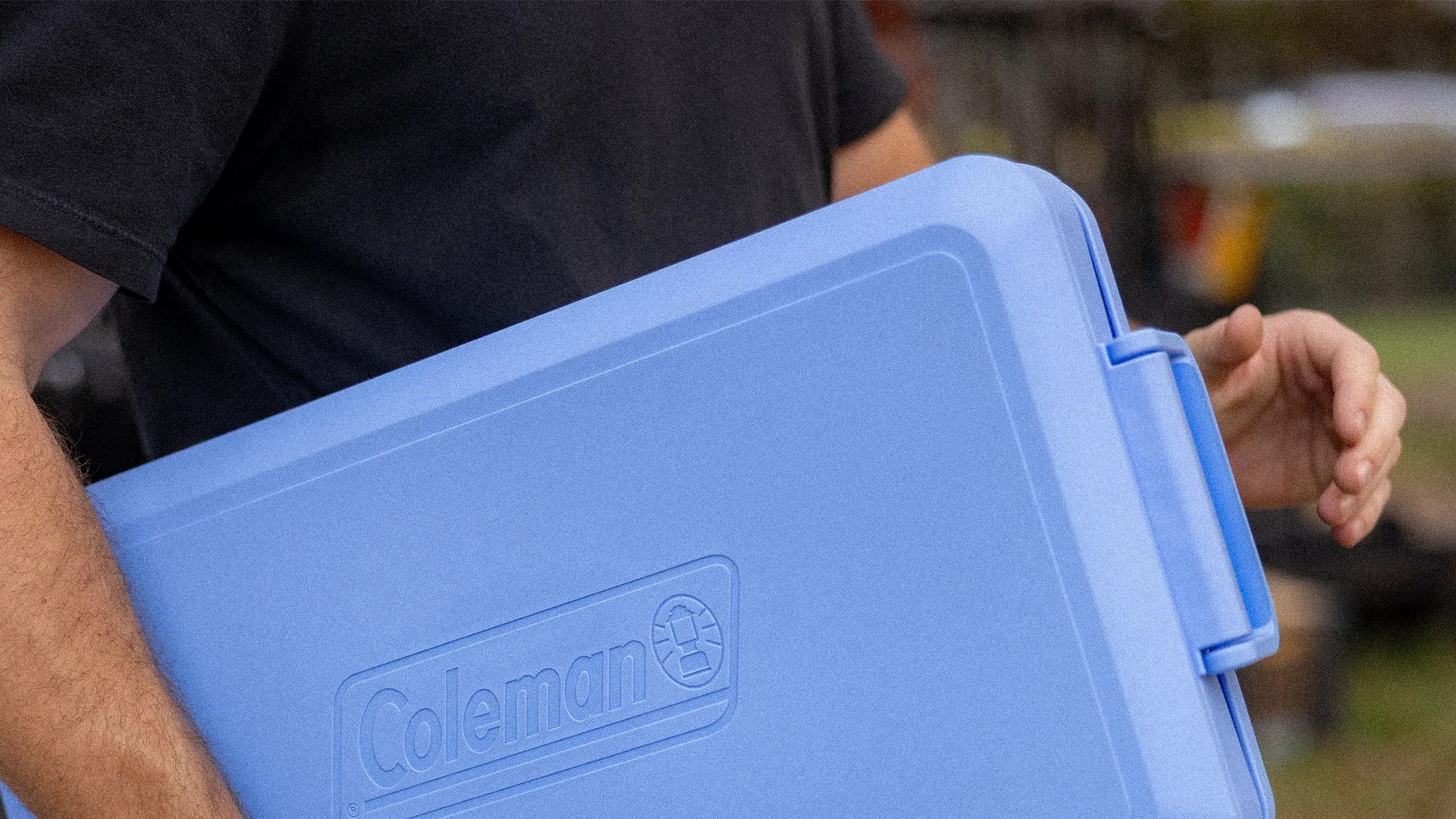 Light blue Coleman cooler with embossed logo held by a person wearing a black shirt.