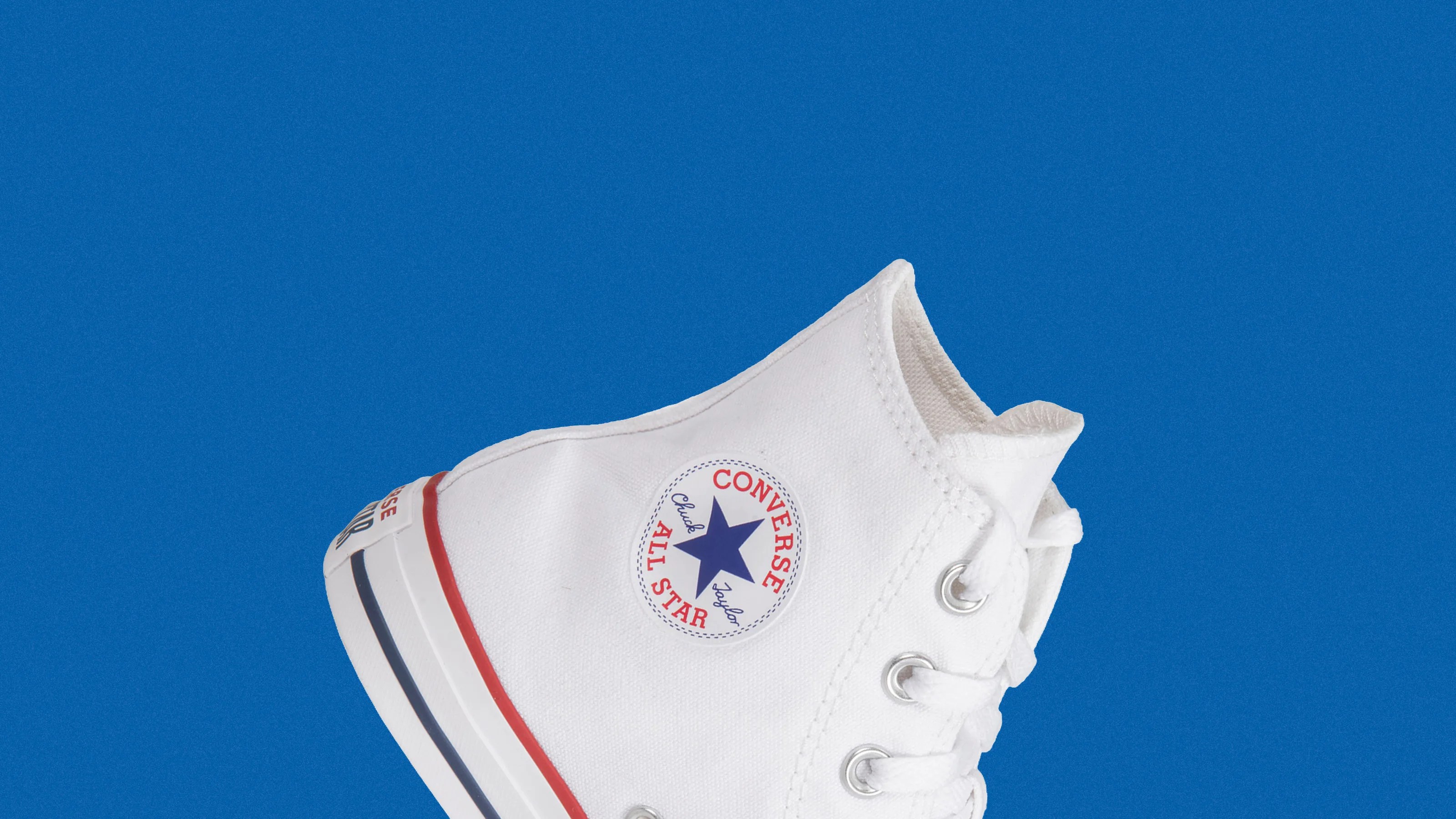 White Converse Chuck Taylor All Star high-top sneaker with red and blue stripes on the sole against a blue background.