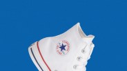 White Converse Chuck Taylor All Star high-top sneaker with red and blue stripes on the sole against a blue background.