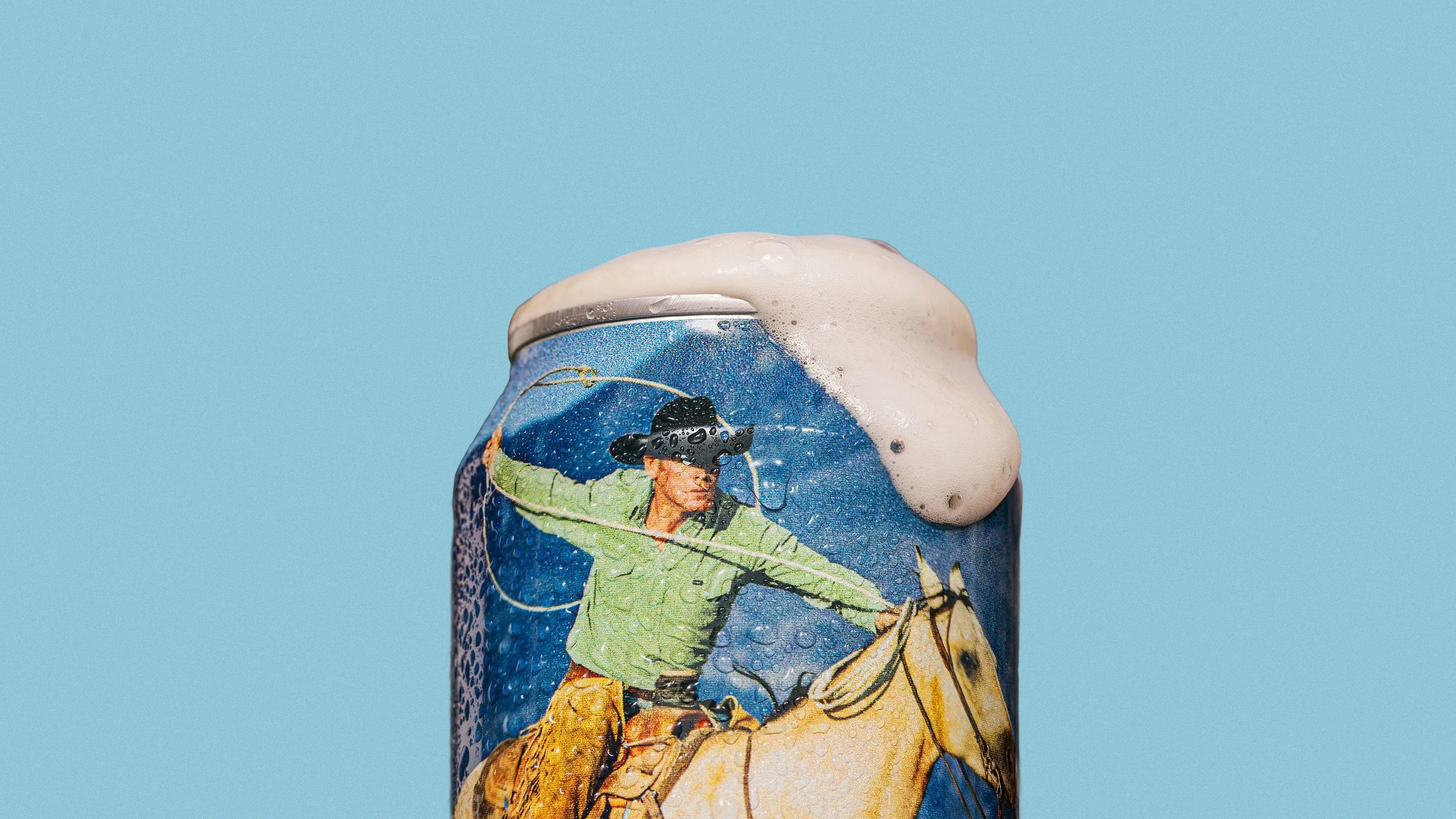 Close-up of a wet beverage can with foam overflowing, featuring a cowboy on horseback illustration.