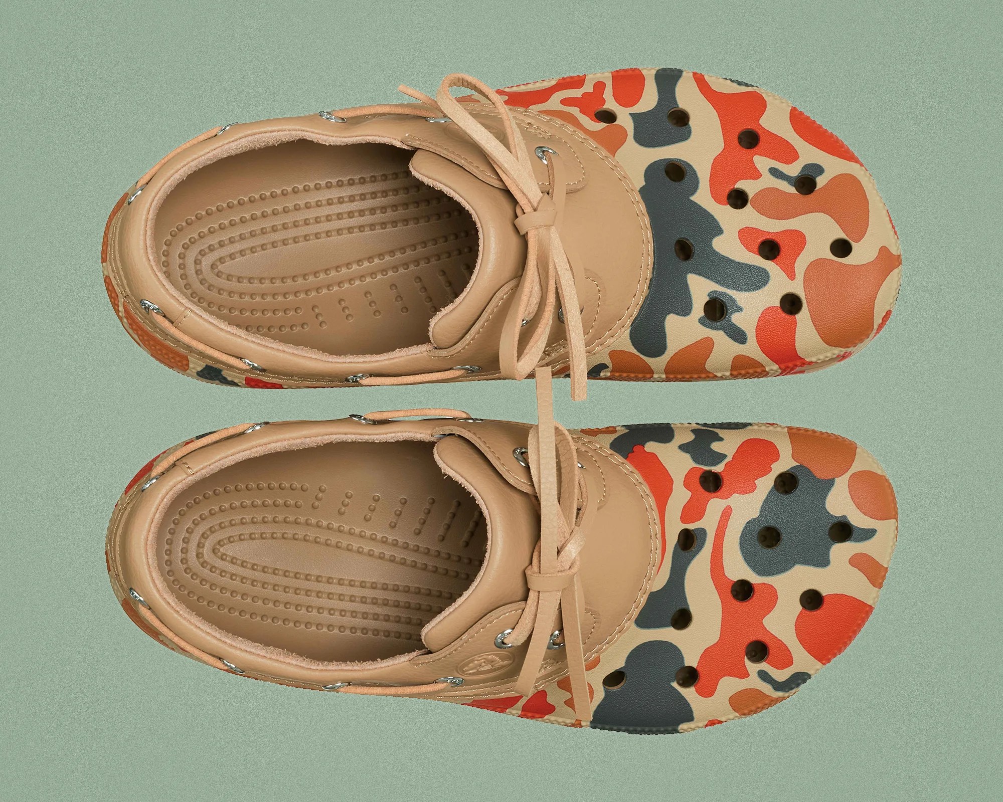Pair of tan leather clogs with orange, black, and beige camouflage pattern and lace-up front on green background.