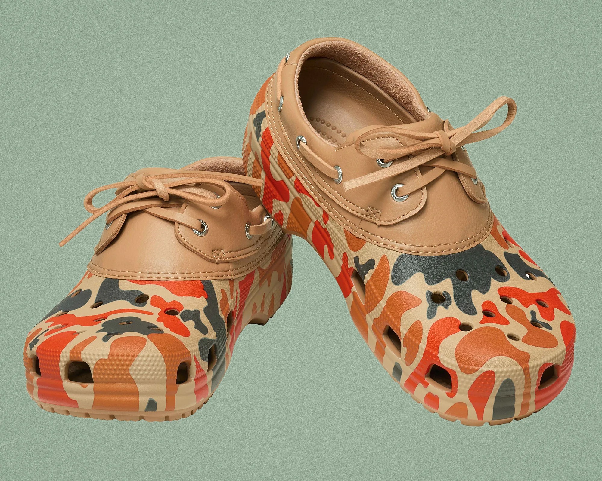 Pair of tan leather and camouflage-patterned rubber clogs with lace-up detail on a green background.