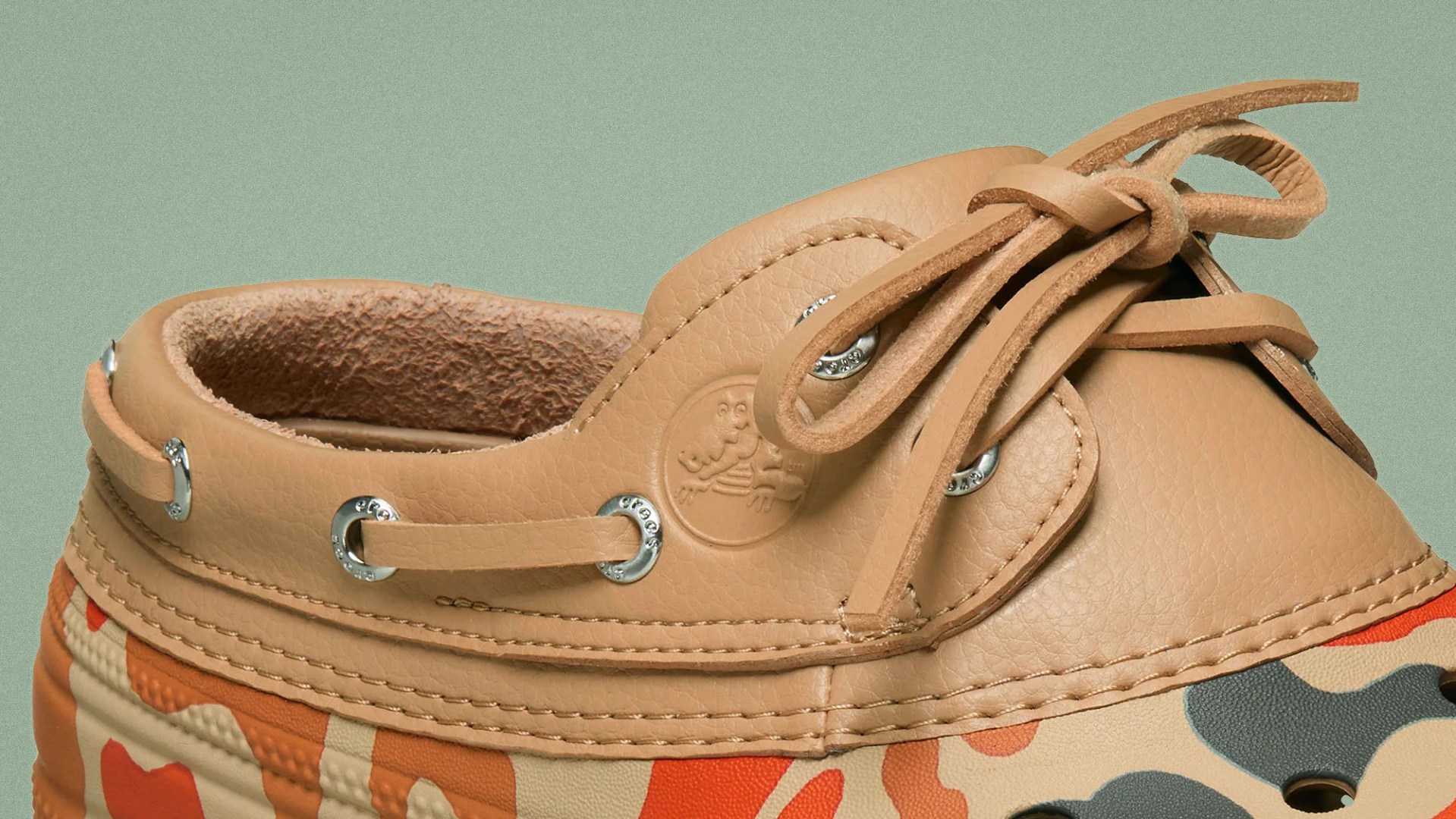 Close-up of a tan leather boat shoe upper with metal eyelets and a multicolor camouflage pattern on the lower part.