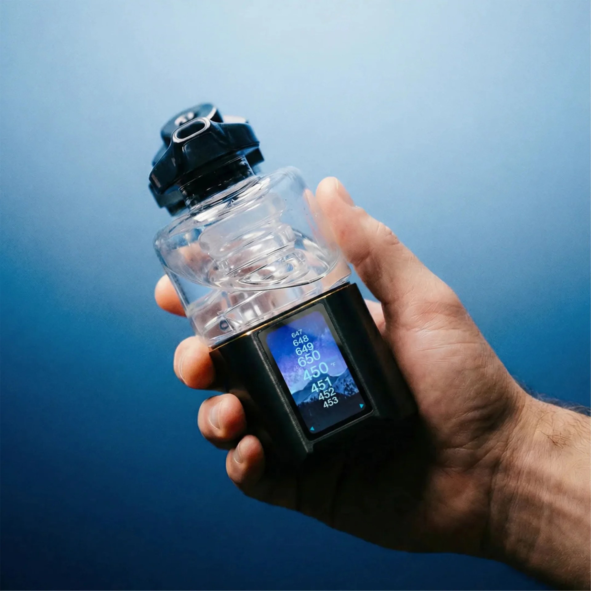 Hand holding a black and clear digital device with a temperature display screen showing numbers in Fahrenheit.