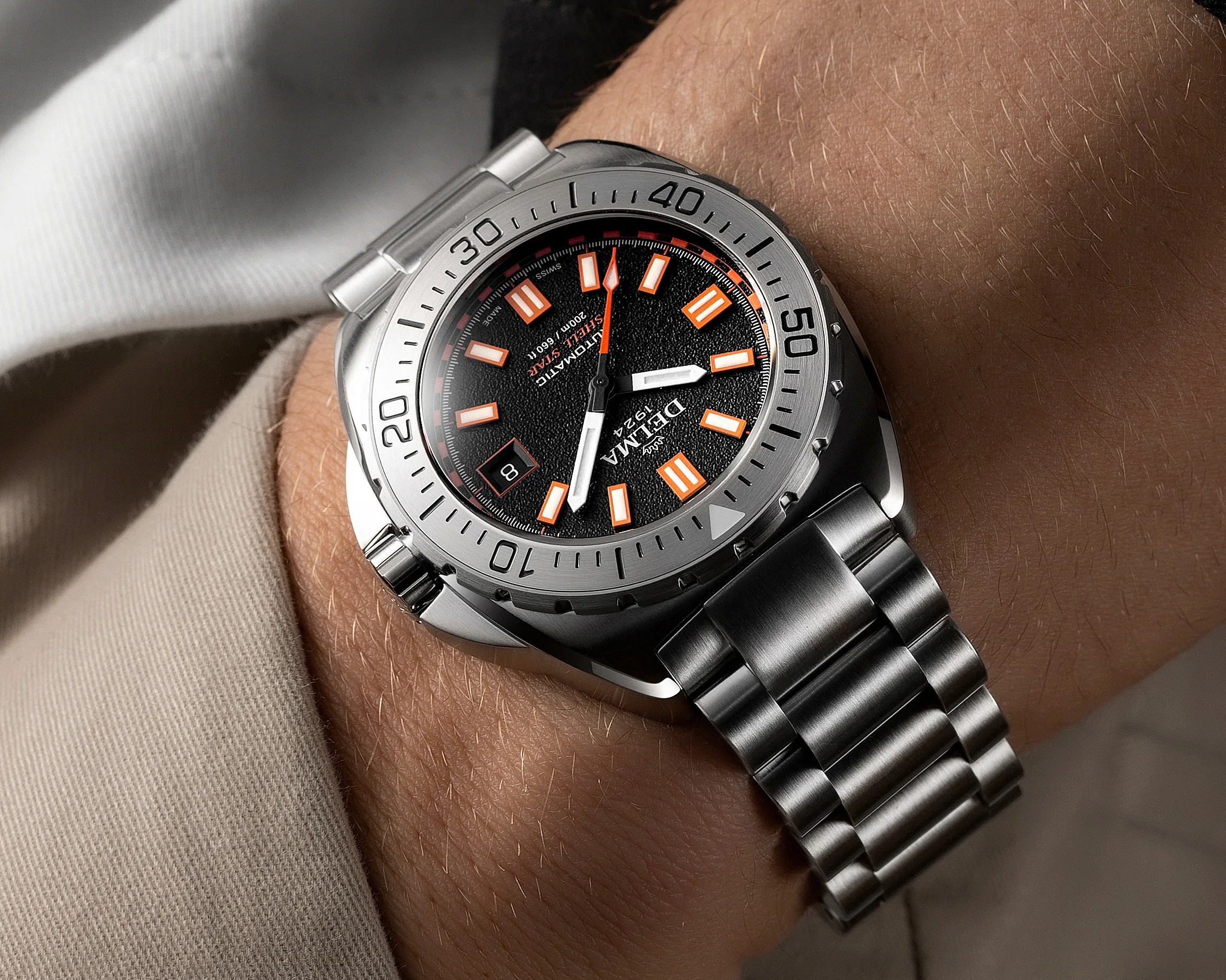 Stainless steel wristwatch with black textured dial and orange-accented hour markers on a wrist.
