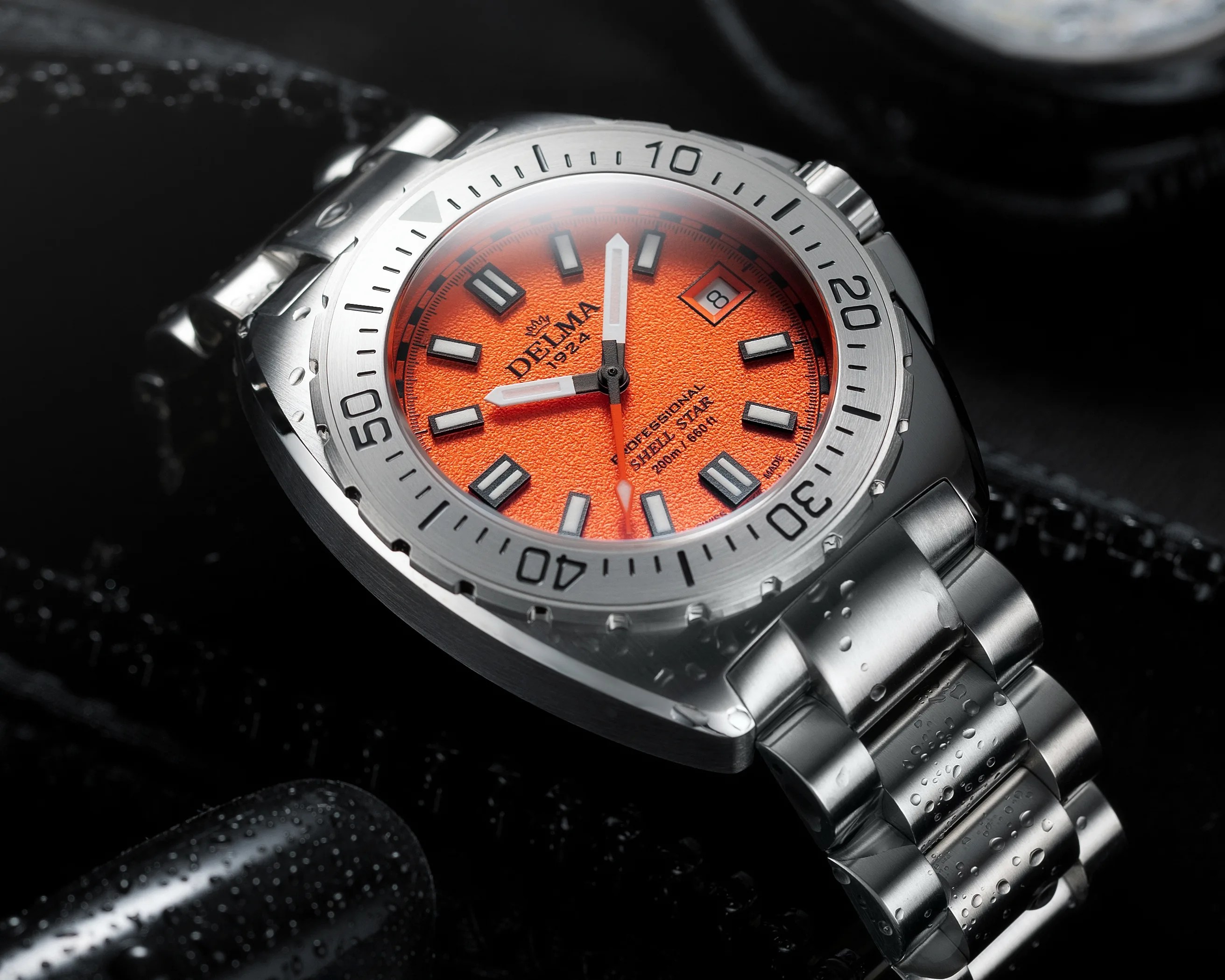 Stainless steel wristwatch with bright orange textured dial and water droplets on the bracelet.