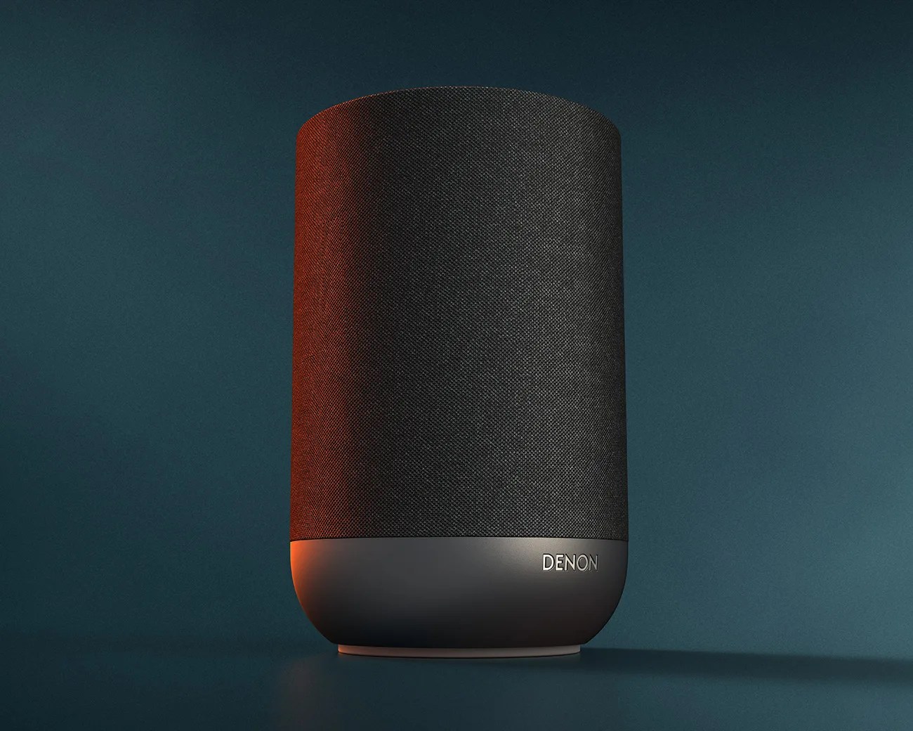 Black cylindrical Denon wireless speaker with fabric cover and matte base on a dark teal surface.