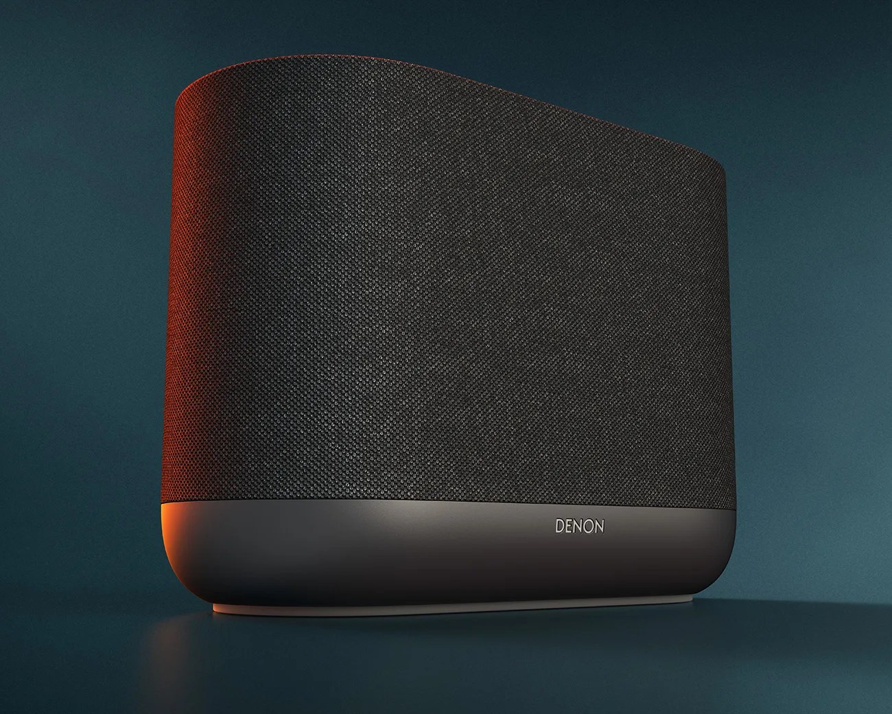 Black Denon wireless speaker with fabric grille and curved edges on a dark surface.
