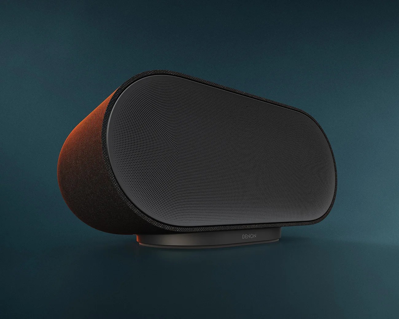 Black Denon wireless speaker with rounded rectangular shape and fabric-covered sides on a dark teal surface.