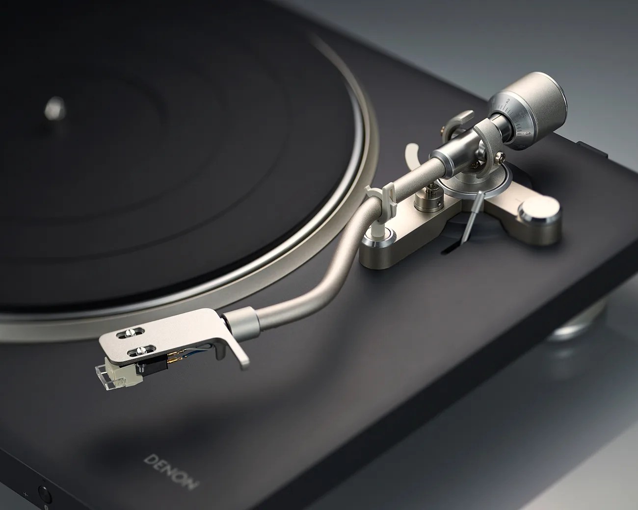 Close-up of a silver tonearm and cartridge on a black Denon turntable.