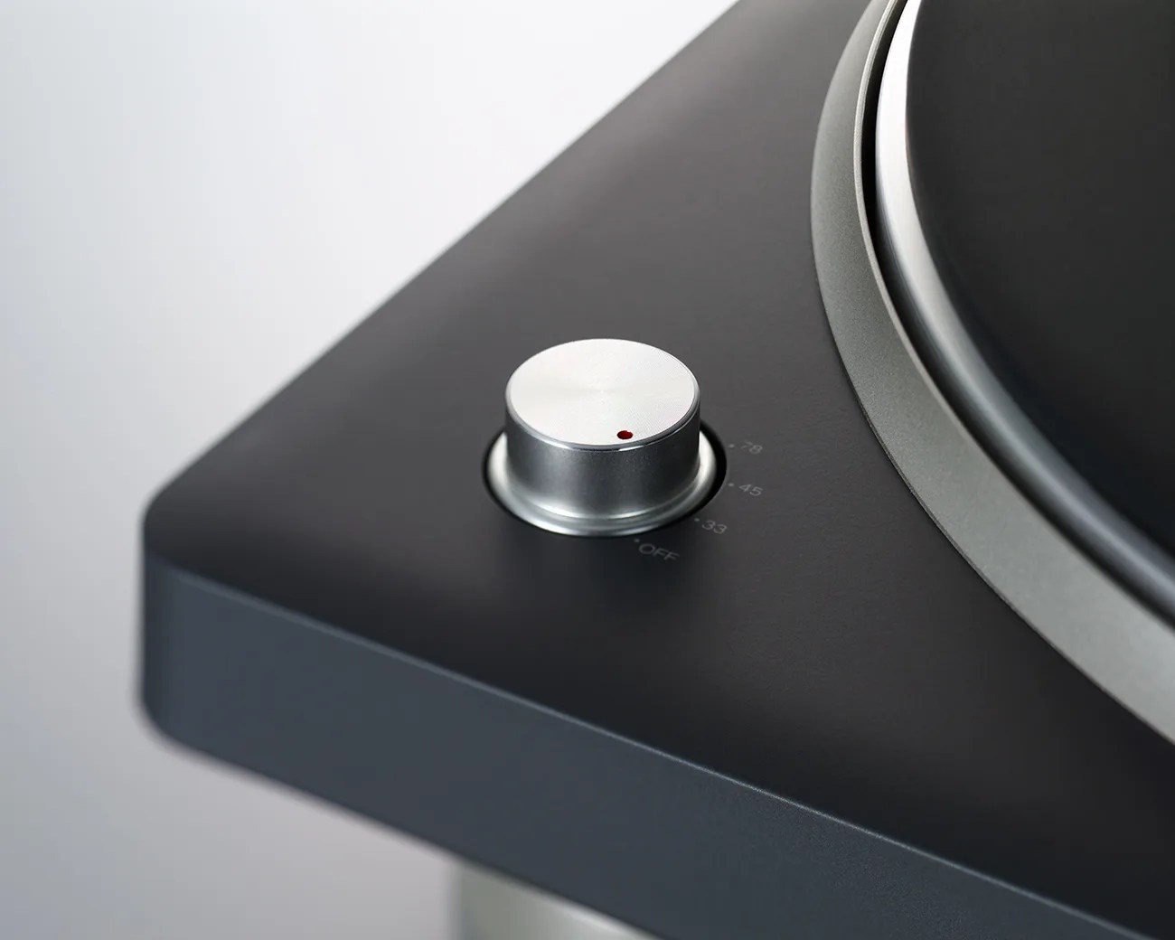 Close-up of a silver control knob with a red indicator on a matte black turntable base.