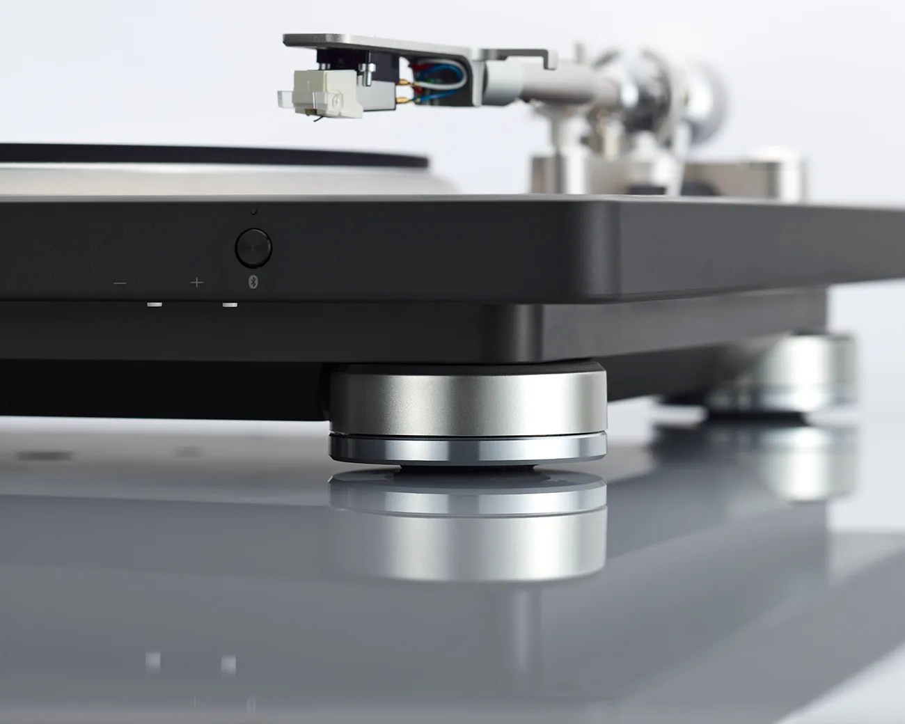 Close-up of a black turntable with silver adjustable feet on a reflective surface.