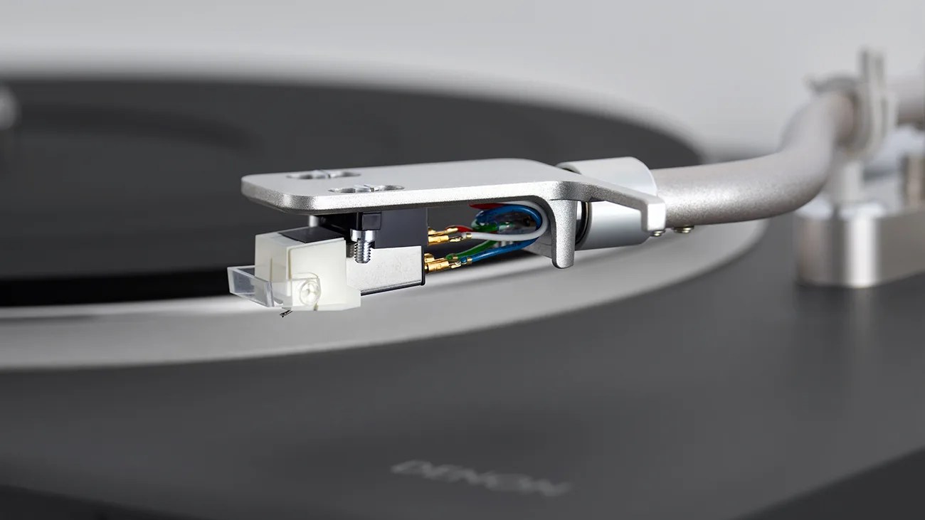 Close-up of a silver tonearm and cartridge with colored wires on a black turntable.