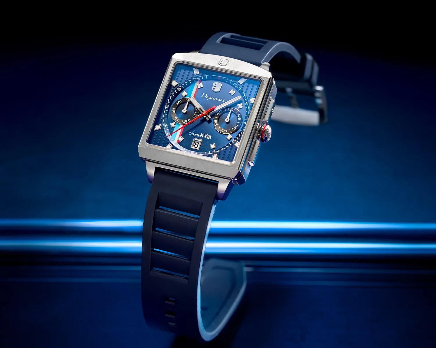 Square stainless steel watch with blue dial, red and white accents, and black rubber strap.